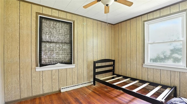 17 E 31st St, Richmond, VA 23224 - unfurnished bedroom with a baseboard radiator, wood walls, wood finished floors, and a ceiling fan
