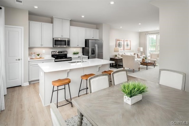 2211 Palm Ct, Sandston, VA 23150 - kitchen with stainless steel appliances, a kitchen bar, a center island with sink, light countertops, and light wood-style flooring