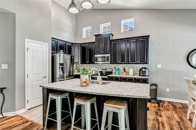 5858 Pilmour Dr, Providence Forge, VA 23140 - kitchen with stainless steel appliances, high vaulted ceiling, dark cabinetry, light wood-style floors, and a kitchen breakfast bar