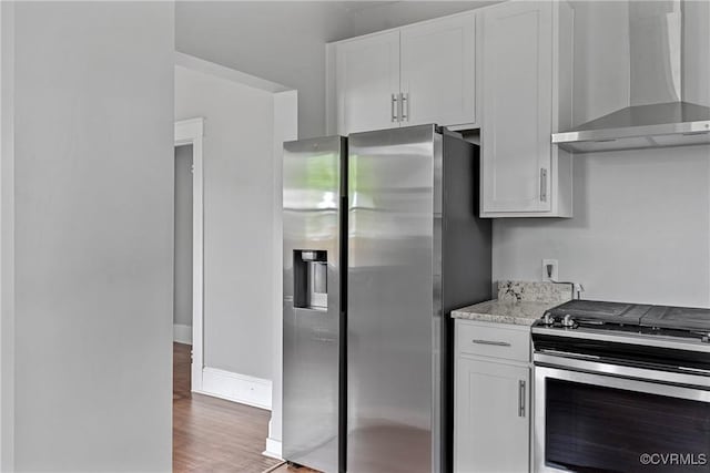 3406 Lawson St, Richmond, VA 23224 - kitchen with wall chimney range hood, stainless steel appliances, light wood finished floors, white cabinetry, and light stone counters