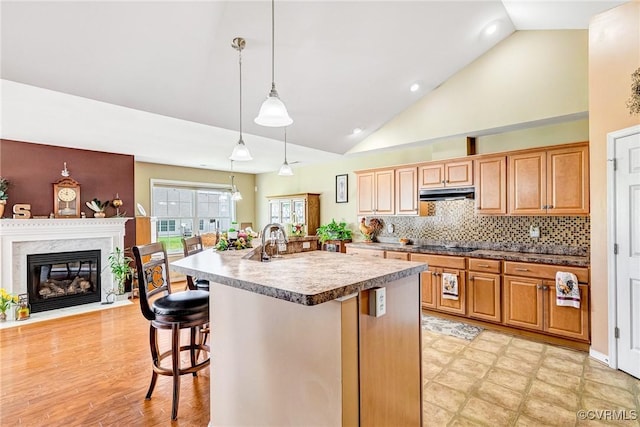 8125 Janice Ave, Mechanicsville, VA 23111 - kitchen with under cabinet range hood, a kitchen island with sink, a breakfast bar, hanging light fixtures, and a premium fireplace