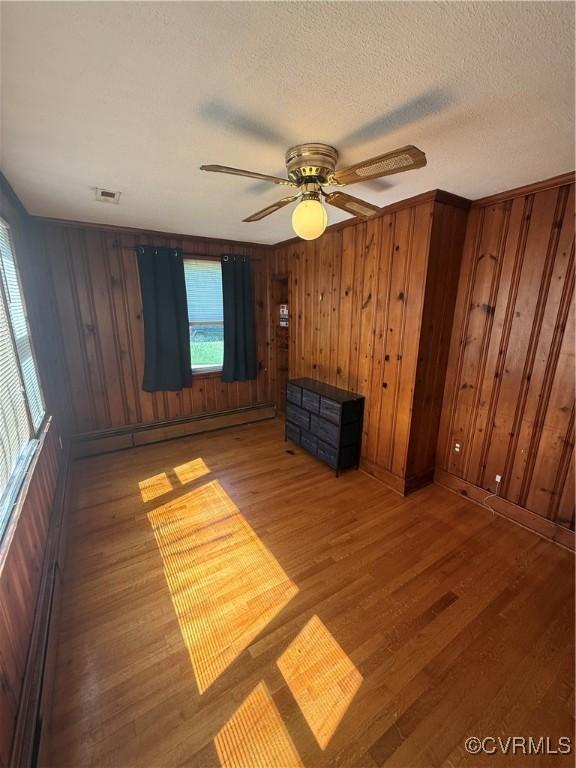 305 Danray Dr, Henrico, VA 23227 - spare room featuring light wood-style flooring, wooden walls, a baseboard radiator, ceiling fan, and a textured ceiling