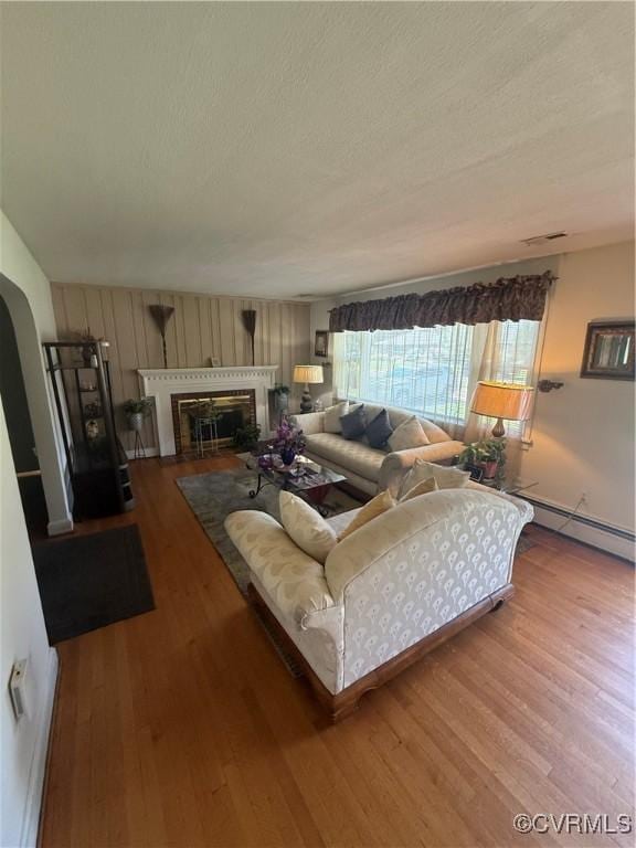 305 Danray Dr, Henrico, VA 23227 - living room with a baseboard heating unit, wood finished floors, a textured ceiling, a glass covered fireplace, and arched walkways