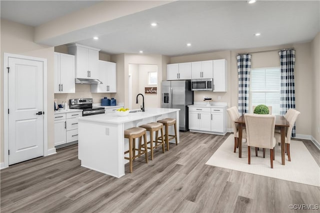 7201 Crosswinds Dr, North Chesterfield, VA 23234 - kitchen featuring stainless steel appliances, under cabinet range hood, a breakfast bar area, light wood finished floors, and a center island with sink