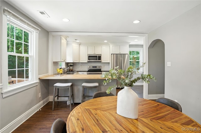 5614 Jahnke Rd, Richmond, VA 23225 - kitchen featuring appliances with stainless steel finishes, dark wood-type flooring, backsplash, a peninsula, and white cabinetry