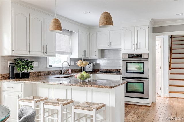 105 Williamson Ct, Henrico, VA 23229 - kitchen with stainless steel double oven, white cabinets, a kitchen breakfast bar, light wood-style floors, and ornamental molding