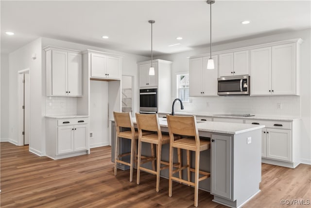9130 Terroir Ln, New Kent, VA 23124 - kitchen featuring appliances with stainless steel finishes, light wood-style floors, a kitchen island with sink, backsplash, and white cabinetry