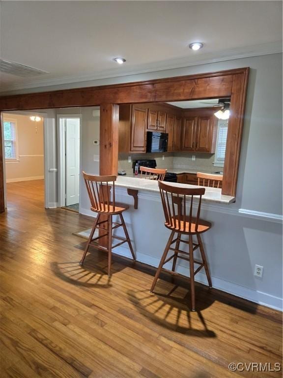 2707 Academy Rd, Powhatan, VA 23139 - kitchen featuring ornamental molding, black microwave, a breakfast bar, wood finished floors, and light countertops