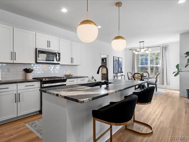 9913 Craftsbury Dr, Midlothian, VA 23112 - kitchen featuring stainless steel microwave, backsplash, light wood-style flooring, a center island with sink, and white cabinetry