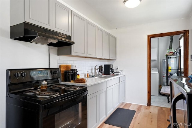 1403 Miles Ave, Hopewell, VA 23860 - kitchen featuring black range with electric cooktop, under cabinet range hood, washer / clothes dryer, light wood-style floors, and backsplash