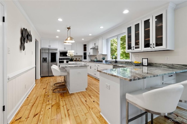 2712 Creek Edge, Powhatan, VA 23139 - kitchen featuring appliances with stainless steel finishes, a breakfast bar area, light wood-style floors, glass insert cabinets, and under cabinet range hood