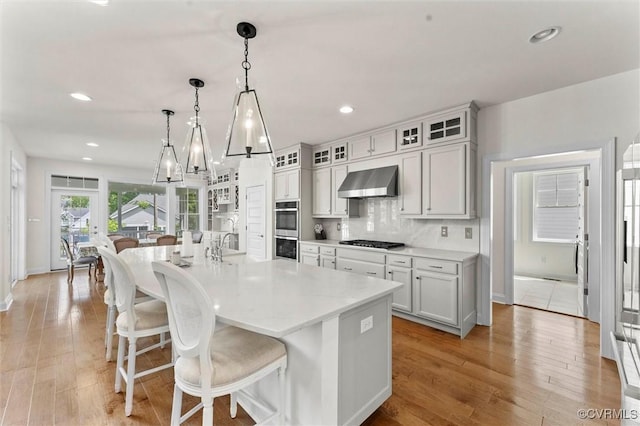 6636 Stonewolf Ct, Moseley, VA 23120 - kitchen featuring wall chimney exhaust hood, stainless steel appliances, a center island with sink, recessed lighting, and a kitchen bar