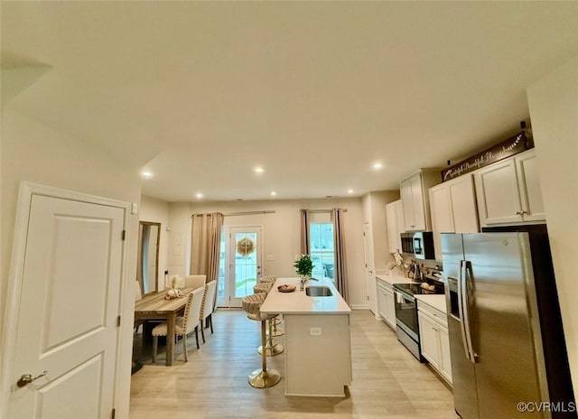 2007 Turtle Pkwy, Henrico, VA 23150 - kitchen featuring appliances with stainless steel finishes, light wood finished floors, a kitchen island with sink, a kitchen breakfast bar, and white cabinetry