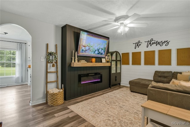 453 Manquin Dr, King William, VA 23009 - living area featuring wood finished floors, ceiling fan, a glass covered fireplace, arched walkways, and a textured ceiling
