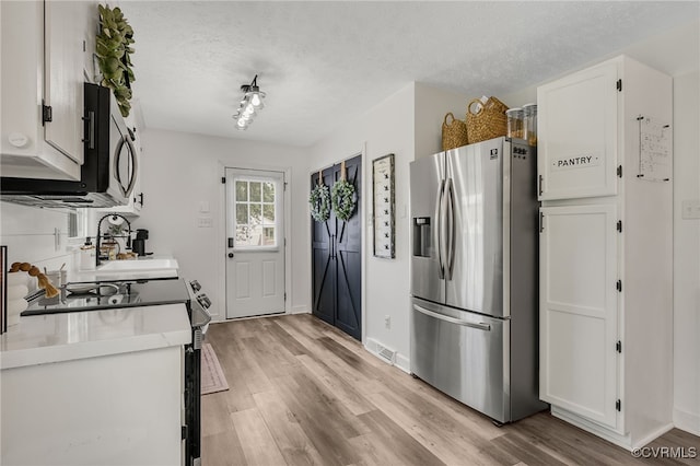 453 Manquin Dr, King William, VA 23009 - kitchen with appliances with stainless steel finishes, light wood finished floors, a textured ceiling, white cabinetry, and light countertops