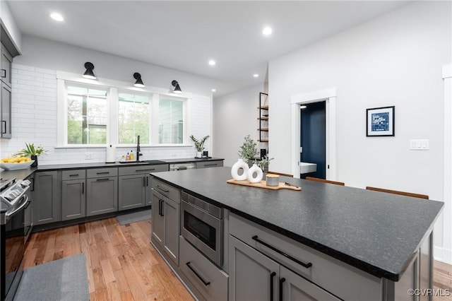 2114 N Ave, Richmond, VA 23222 - kitchen featuring appliances with stainless steel finishes, dark countertops, gray cabinetry, decorative backsplash, and light wood finished floors