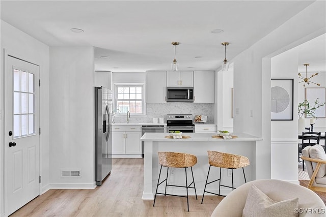 1908 Windsordale Dr, Henrico, VA 23229 - kitchen featuring appliances with stainless steel finishes, a peninsula, backsplash, light wood-style floors, and a kitchen breakfast bar