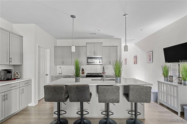 7001 Leire Ln, Chesterfield, VA 23832 - kitchen featuring stainless steel microwave, decorative backsplash, gray cabinetry, a kitchen bar, and light countertops