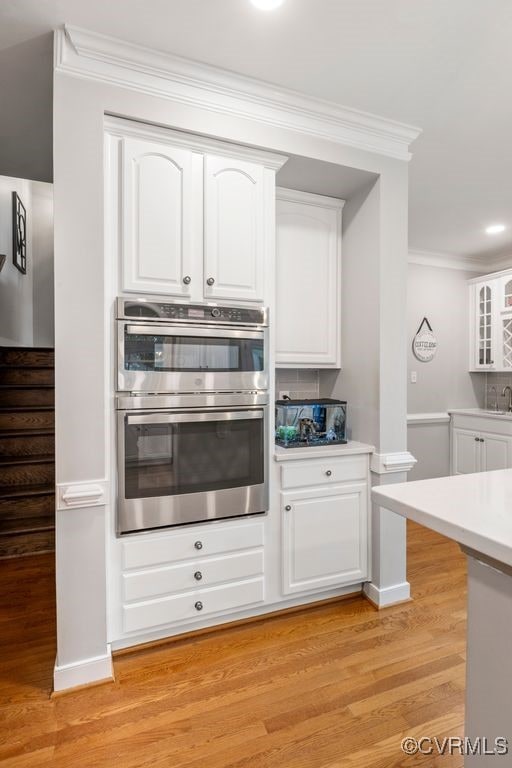 15585 Fox Cove Cir, Moseley, VA 23120 - kitchen with white cabinetry, light wood-style flooring, stainless steel double oven, ornamental molding, and light countertops