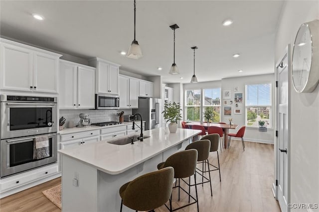 2133 Cantina Ln, Midlothian, VA 23114 - kitchen with stainless steel appliances, a breakfast bar area, an island with sink, light wood-style floors, and white cabinets