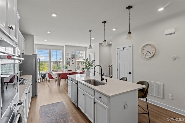 2133 Cantina Ln, Midlothian, VA 23114 - kitchen with stainless steel appliances, an island with sink, light wood-style floors, white cabinets, and light countertops