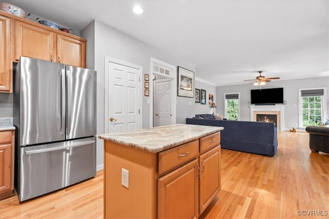 24000 Pear Orchard Rd, Moseley, VA 23120 - kitchen with freestanding refrigerator, light wood-type flooring, a ceiling fan, a warm lit fireplace, and a kitchen island