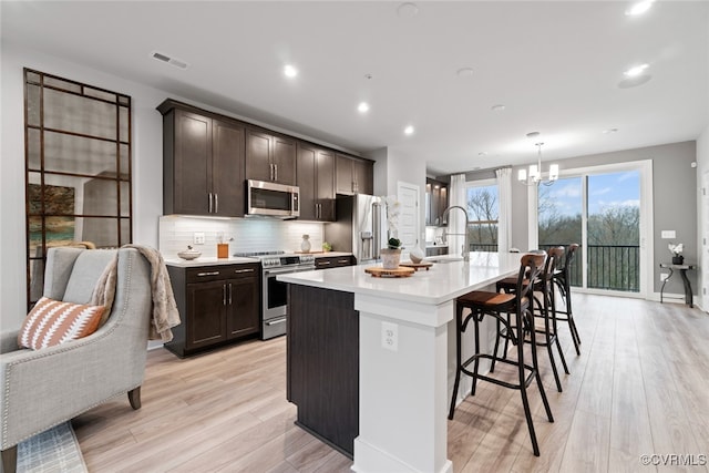 13213 Garland Ln, Midlothian, VA 23114 - kitchen with appliances with stainless steel finishes, dark brown cabinets, a kitchen bar, light wood-style flooring, and recessed lighting