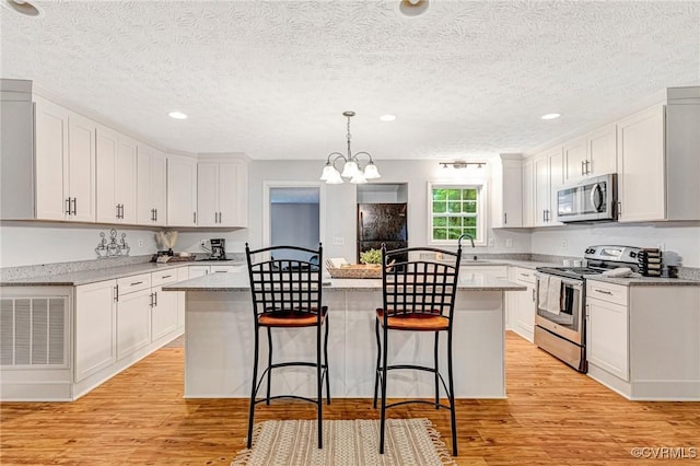 9118 Epps Rd, Mechanicsville, VA 23111 - kitchen featuring appliances with stainless steel finishes, a kitchen island, a textured ceiling, white cabinets, and light wood-style flooring