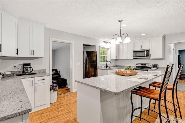 9118 Epps Rd, Mechanicsville, VA 23111 - kitchen with appliances with stainless steel finishes, light wood-type flooring, a breakfast bar, white cabinets, and a textured ceiling