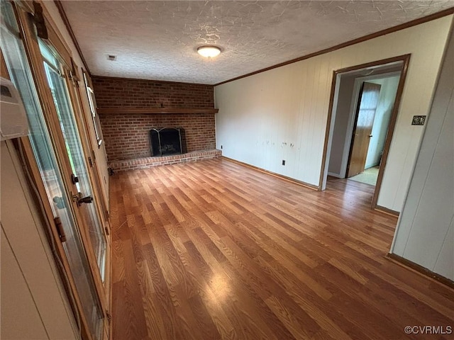 unfurnished living room featuring ornamental molding, wood finished floors, a brick fireplace, and a textured ceiling