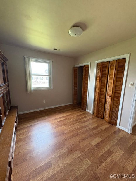 unfurnished bedroom with two closets and light wood finished floors