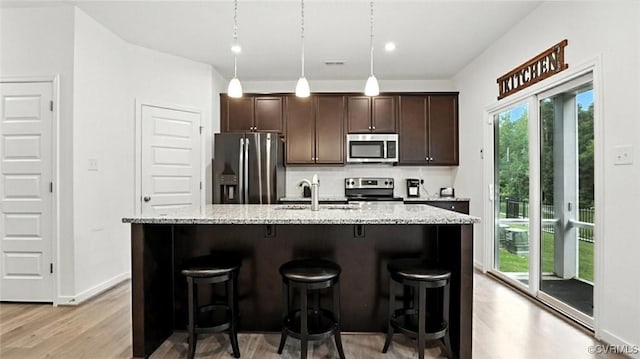 7750 Leeds Castle Ln, New Kent, VA 23124 - kitchen featuring appliances with stainless steel finishes, light wood-style floors, dark brown cabinets, a kitchen island with sink, and a breakfast bar area