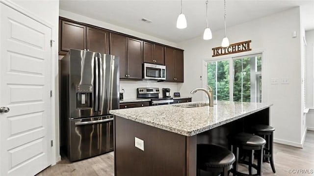 7750 Leeds Castle Ln, New Kent, VA 23124 - kitchen featuring appliances with stainless steel finishes, light wood finished floors, a breakfast bar area, dark brown cabinets, and light stone counters