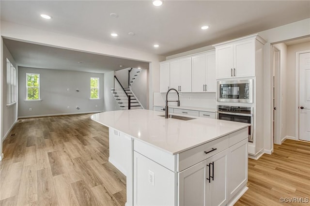 7127 Braxton Ct, Ladysmith, VA 22546 - kitchen featuring stainless steel appliances, open floor plan, light wood-type flooring, white cabinetry, and a center island with sink