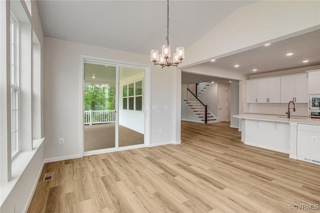 7127 Braxton Ct, Ladysmith, VA 22546 - kitchen featuring light countertops, vaulted ceiling, white cabinetry, light wood-style flooring, and hanging light fixtures