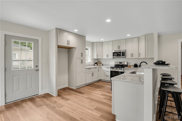 407 S 19th Ave, Hopewell, VA 23860 - kitchen with stainless steel appliances, a peninsula, a breakfast bar, light wood-style flooring, and light stone countertops