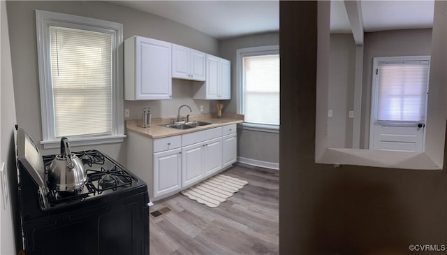 1883 Fairfax St, Petersburg, VA 23805 - kitchen with black range with gas cooktop, light countertops, light wood-type flooring, and white cabinetry
