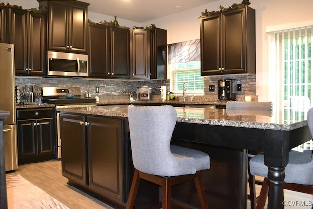 4331 Ganymede Dr, Chester, VA 23831 - kitchen featuring stainless steel appliances, a breakfast bar area, decorative backsplash, stone countertops, and light wood-style floors
