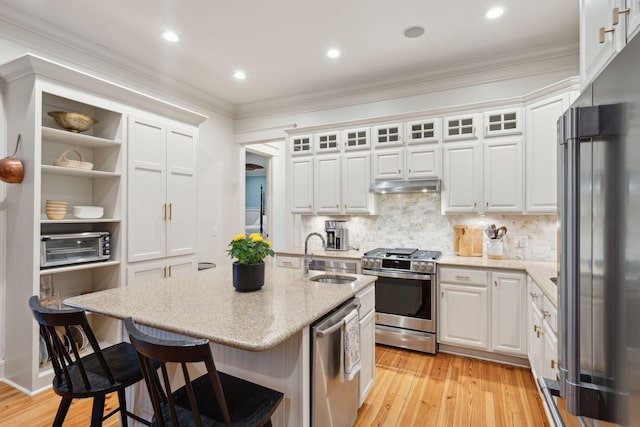 kitchen with sink, appliances with stainless steel finishes, a kitchen island with sink, white cabinets, and a kitchen bar