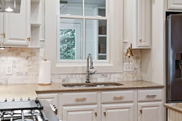 kitchen featuring stainless steel refrigerator with ice dispenser, sink, light stone counters, and white cabinets