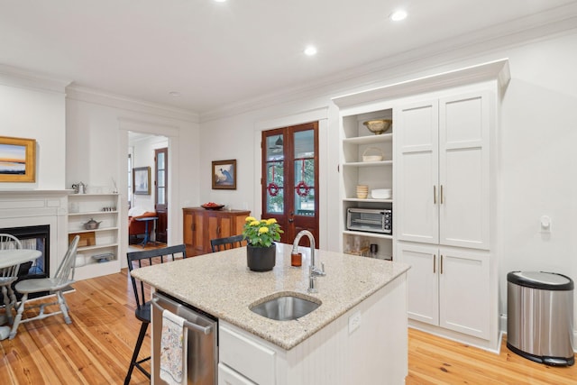 kitchen with sink, white cabinetry, crown molding, light stone counters, and a kitchen island with sink