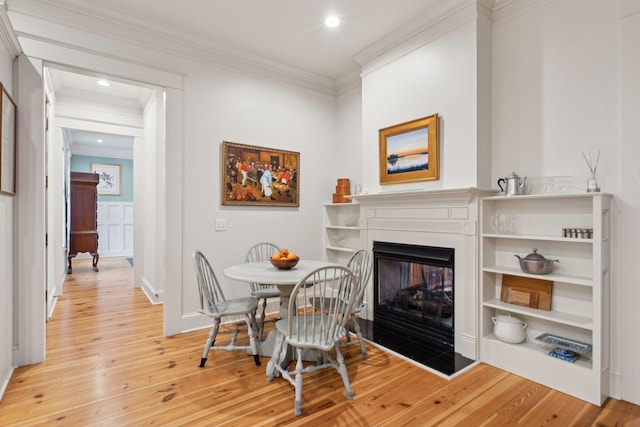 dining room with a multi sided fireplace, ornamental molding, and light wood-type flooring