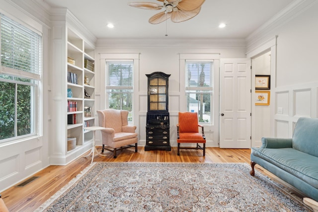 living area with wood-type flooring, ornamental molding, and ceiling fan