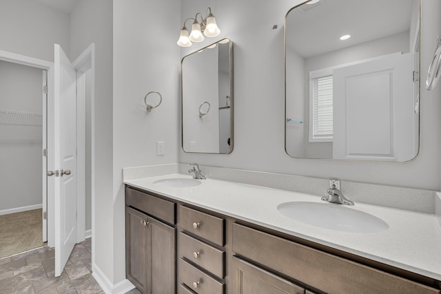 bathroom featuring double vanity, baseboards, stone finish flooring, and a sink