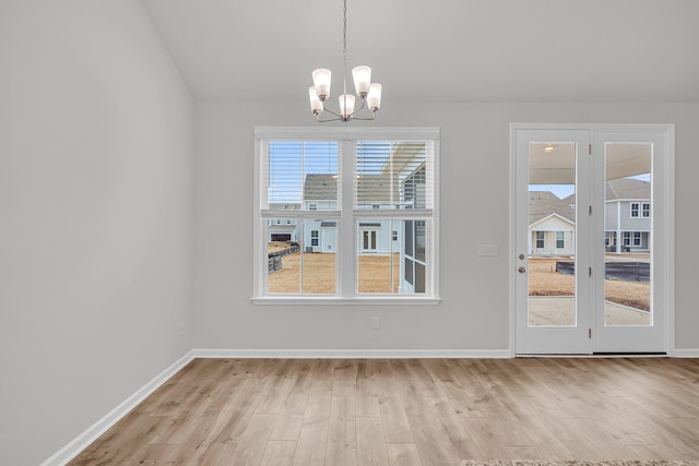 unfurnished dining area featuring a notable chandelier, baseboards, and wood finished floors