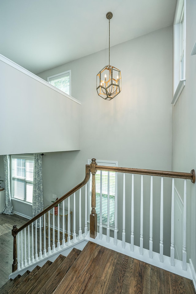 staircase with a towering ceiling, a chandelier, and wood-type flooring