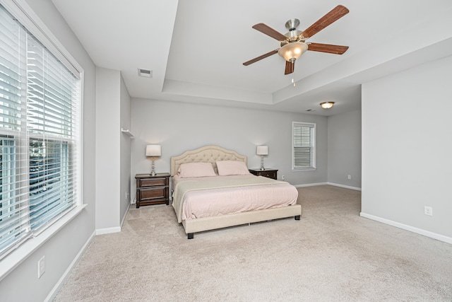 carpeted bedroom with multiple windows, a tray ceiling, and ceiling fan