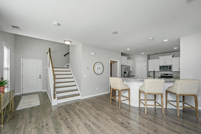 kitchen with light stone countertops, appliances with stainless steel finishes, a kitchen bar, hardwood / wood-style floors, and white cabinets