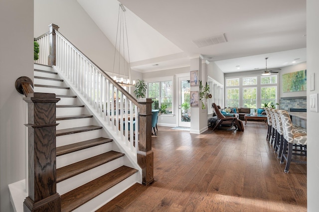 stairway featuring hardwood / wood-style floors, a stone fireplace, ceiling fan with notable chandelier, and a towering ceiling