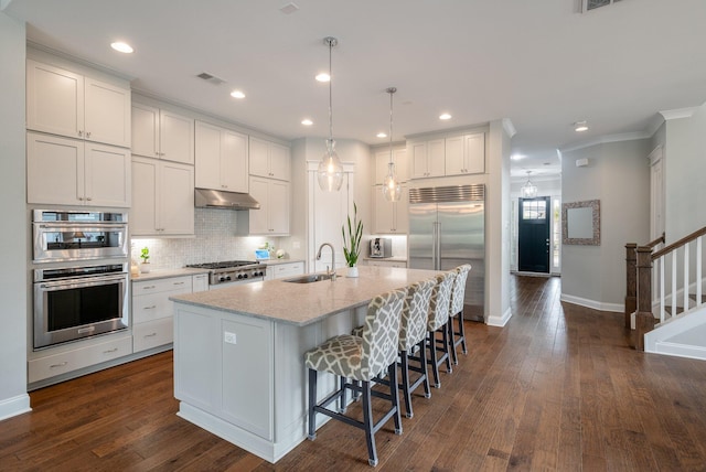 kitchen with an island with sink, white cabinetry, sink, hanging light fixtures, and stainless steel appliances